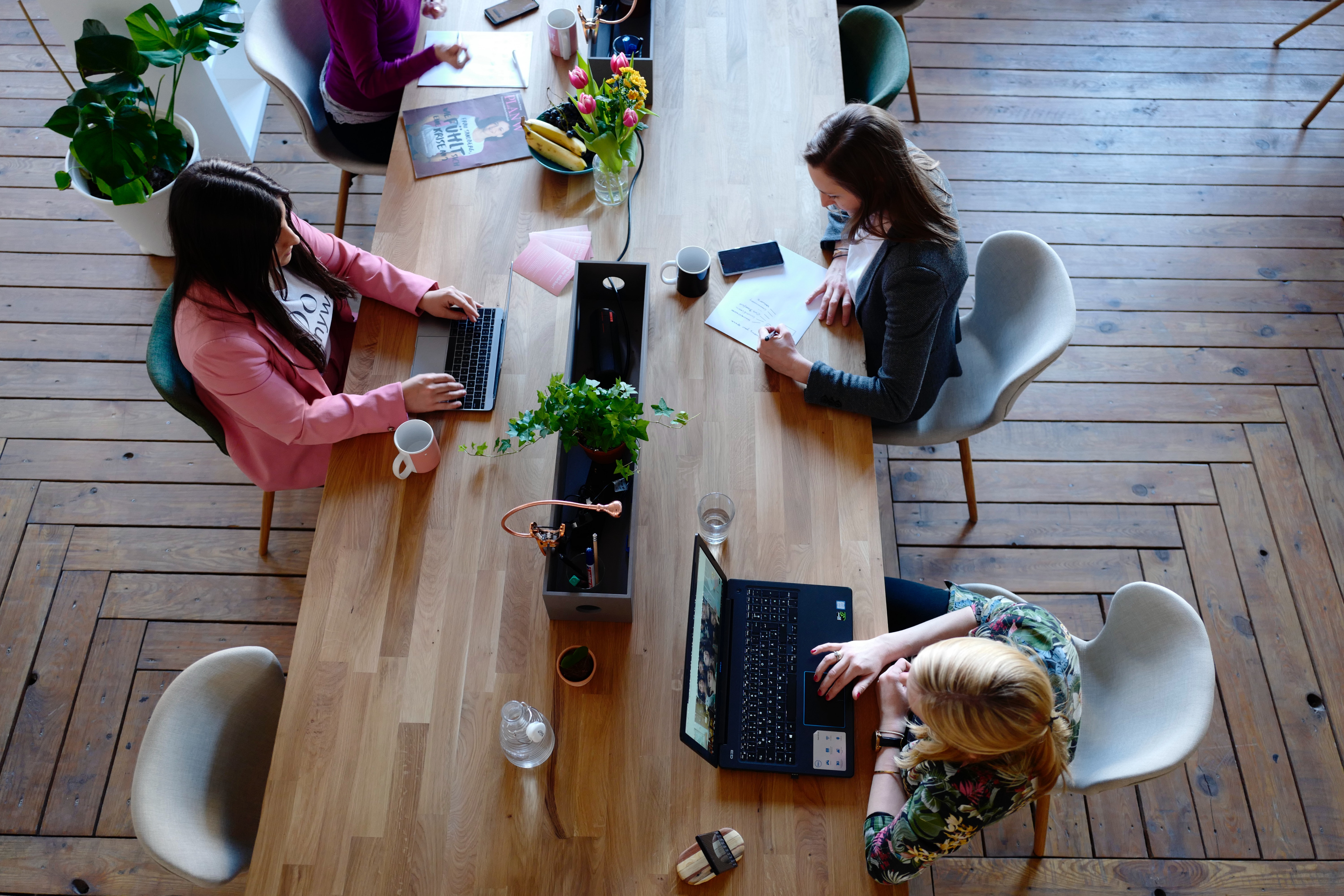 three women working in an office space around a wooden desk